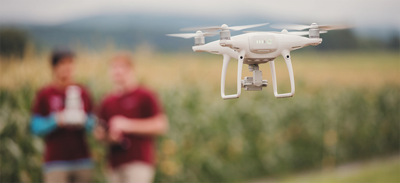 Image of two students flying a drone over a field